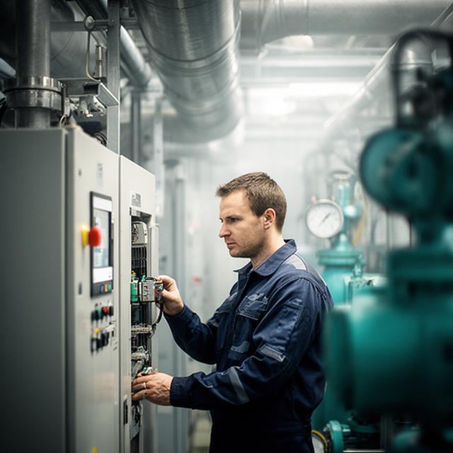 Engineer checking plant controls beside a compressor room in a UK factory